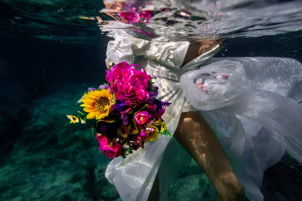 Underwater bride with flowers in a white dress in dark blue water, mediterranean sea