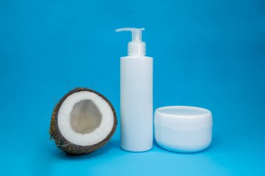Beyaz kozmetik şişesi ve kavanozla hindistan cevizi, mavi arka planda kozmetik ürünü. Minimum konsept. Sunum için sunum cilt ürünleri
