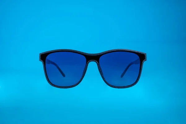 Солнечные очки с синим стеклом и черной рамкой на синем фоне — стоковое фото