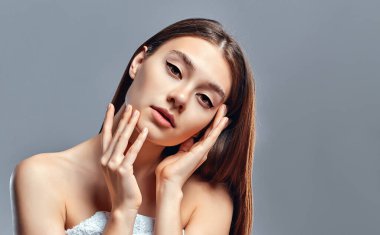 Temiz ciltli güzel bir genç kadın. Doğal çıplak makyajlı bir güzellik modeli. Spa, cilt bakımı ve sağlık. Kapat, gri arkaplan, telif alanı.