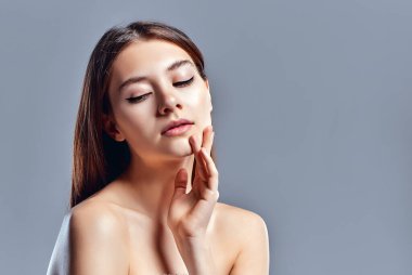 Temiz ciltli güzel bir genç kadın. Doğal çıplak makyajlı bir güzellik modeli. Spa, cilt bakımı ve sağlık. Kapat, gri arkaplan, telif alanı.