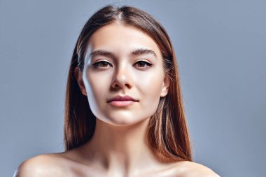 Temiz ciltli güzel bir genç kadın. Doğal çıplak makyajlı bir güzellik modeli. Spa, cilt bakımı ve sağlık. Kapat, gri arkaplan, telif alanı.