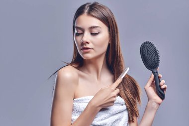 Güzel, çekici ve bakımlı bir kadının portresi elinde tarak, yumuşak, ipeksi saçlar, keratin etkisi, gri arka planda izole edilmiş..