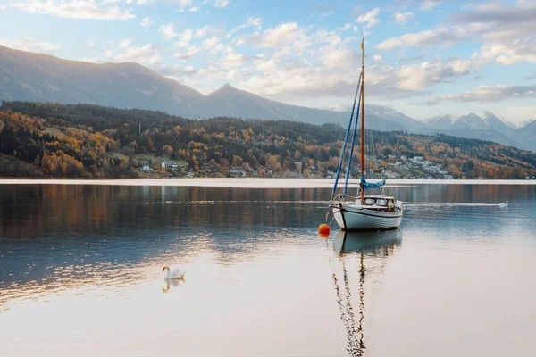 Sailboat at the idyllic lake Millstaetter See in Carinthia, Austria. Beautiful alpine lake in autumn with snow covered mountains in the background.