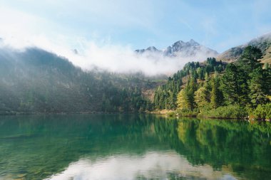 A tranquil mountain lake surrounded by alpine peaks and lush nature, reflecting the beauty of the Austrian Alps near Kleiner Scheibelsee on a clear day.