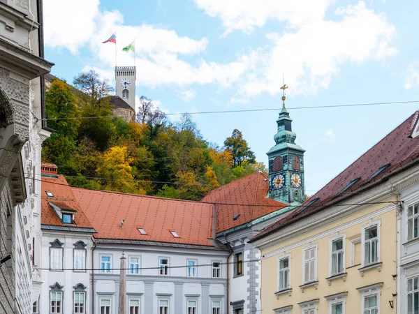 Ljubljana 'nın eski şehir merkezi tepedeki tarihi belediye kulesini ve Ljubljana Kalesini gösteriyor, sonbahar yapraklarıyla çevrili..