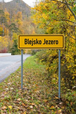 Slovenya 'nın ünlü dağlık kesiminin girişini sembolize eden, rengarenk sonbahar ağaçlarıyla çevrili sarı Bled yol tabelasına yakın plan..