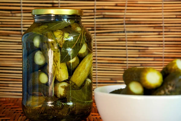 Pickled cucumbers in a jar of spices and a small white bowl with pickled cucumbers in the foreground. — Stock Photo, Image