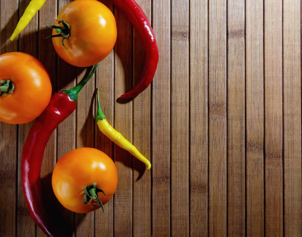 Tomates amarelos e pimentas estão em um fundo de madeira. — Fotografia de Stock