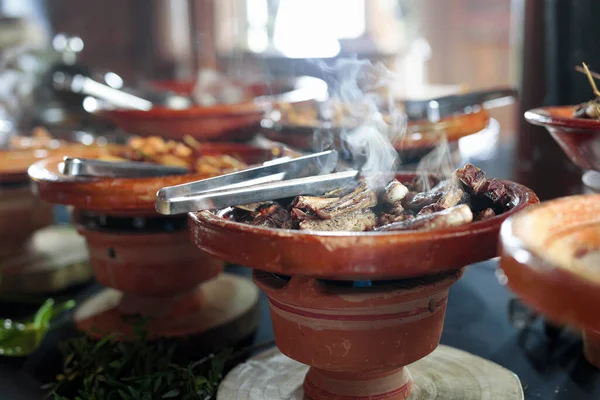 Cooked Belgian food placed in ceramic containers with a fire underneath to keep it warm.