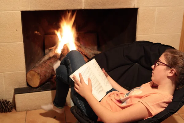 Chica leyendo un libro en la chimenea Fotos De Stock