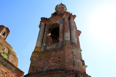 Parlak bir gökyüzüne karşı harap olmuş eski bir tuğla binanın kulesi..