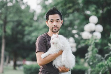 Parkta beyaz bir kedi tutan adam.