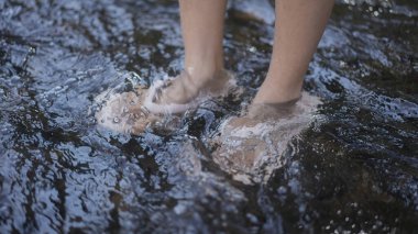 Çıplak ayakların ve alt bacaklarının yakın çekimi, sığ, berrak suda yüzen dalgalar ve sıçramalar, açık hava doğa rahatlama konsepti..