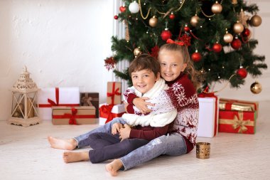 Noel ağacının altında oturan çocuk gülümseyen