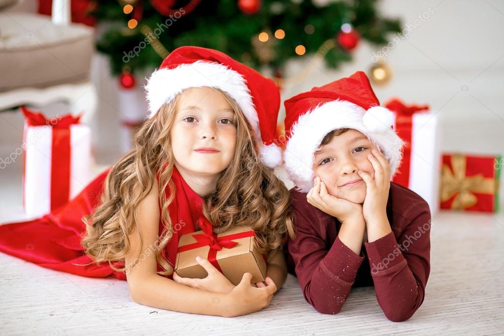 Children wearing Santa Claus sitting with gifts under the Christmas tree