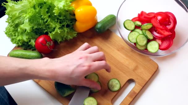 Människohänder klippa och sätta i en sallad skål gurka. — Stockvideo