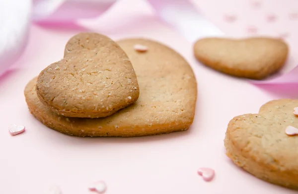 Sladké sušenky ve tvaru srdce pro den svatého Valentýna na růžovém pozadí s mašlí. — Stock fotografie