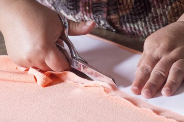 Kadının elleri makasla kumaş kesiyor.