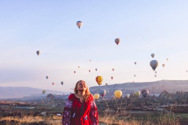 Ukraynalı kırmızı elbiseli güzel bir kız Kapadokya 'da şafak vakti gülerken balonlar havada uçuşuyor.