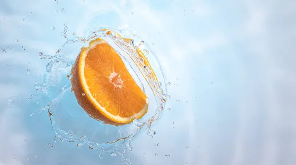 Fresh ripe half of orange fruit splashing into clear water.