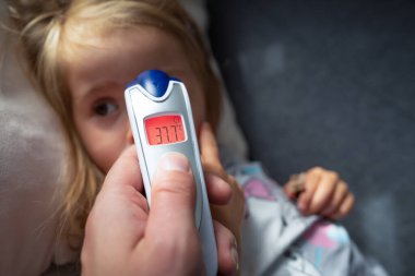 Anne, evde kızıl ötesi termometresi olan çocuğu için ateşini ölçüyor. Annesi dijital kızılötesi termometreyi tutuyor..