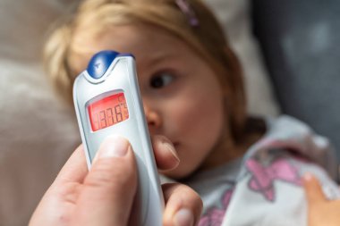 Anne, evde kızıl ötesi termometresi olan çocuğu için ateşini ölçüyor. Annesi dijital kızılötesi termometreyi tutuyor..