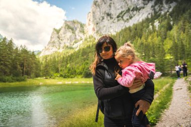 Genç bir anne, Gruner etrafında yürürken çocuğu tutuyor. Avusturya, Styria 'da yeşil bir göl görüyor. Aile kavramı ile yürüyüş.