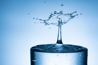 İzole edilmiş parlak mavi arkaplandan su damlası cama sıçrıyor.