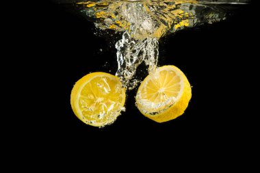 Suda taze sarı limon parçaları. Siyah arka planda izole edilmiş su sıçraması..
