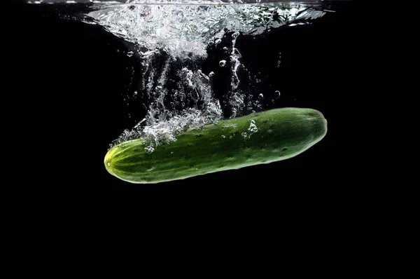 Groene bio komkommer zinken onder water tegen zwarte achtergrond — Stockfoto