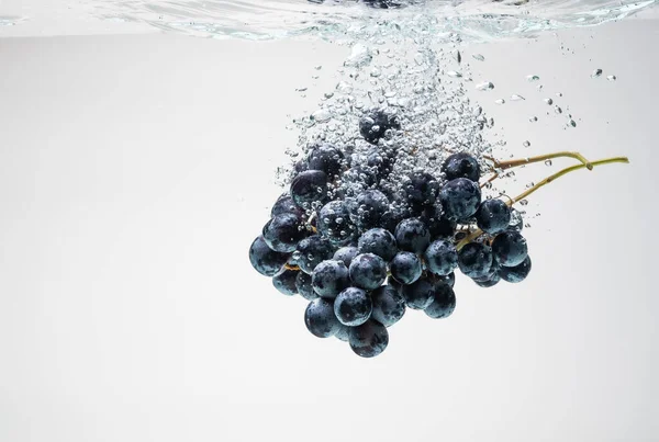 Bando de uvas azuis a afundar-se debaixo de água com salpicos. — Fotografia de Stock