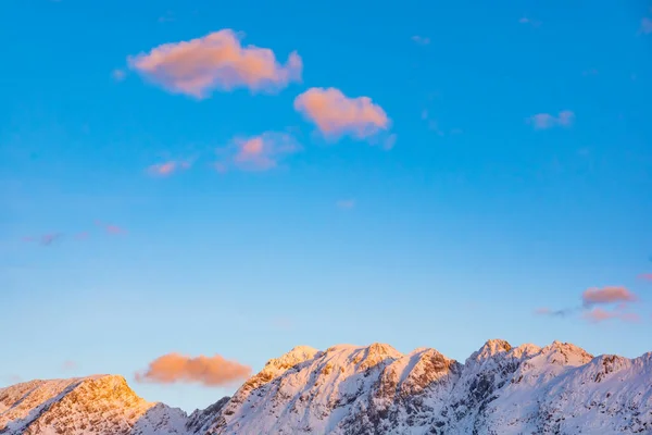 Picos de montaña durante la puesta del sol contra el cielo azul con nubes esponjosas naranjas. — Foto de Stock