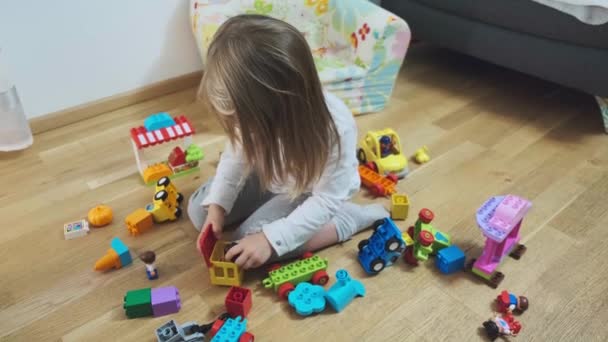 Schattig klein meisje zit op de vloer en spelen met kleurrijke bouwstenen. — Stockvideo