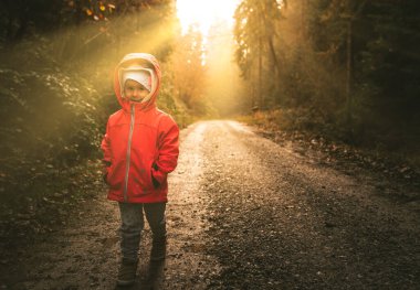Karamsar ormanda ıslak yolda duran bir çocuk.