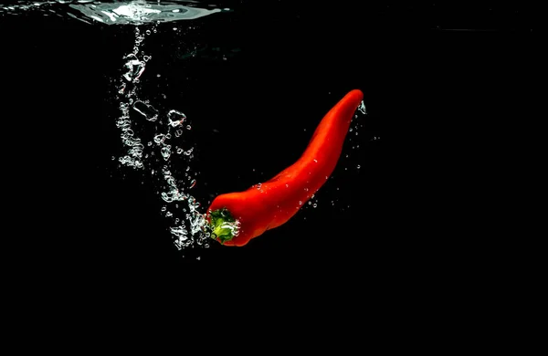Red pepper falls to the water, causing bubbles and scattered water. — Stock Photo, Image