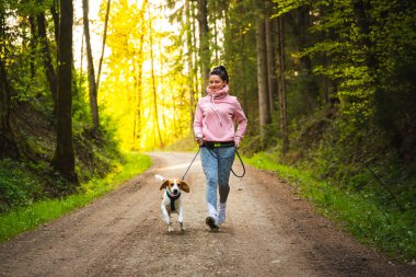 Genç kadın ve köpek güneşli ormanda birlikte koşuyorlar..