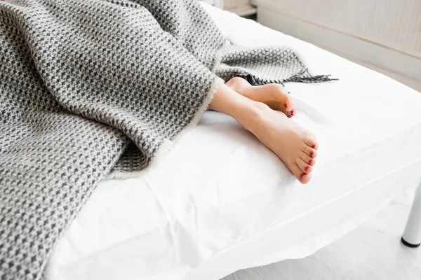 Woman feet under gray blanket sideview — Stock Photo, Image