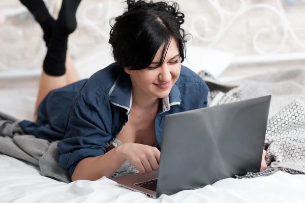 Donna sorridente sul letto con computer portatile — Foto Stock