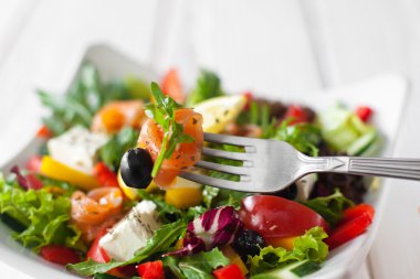 Çatalla füme somon yiyen sebze salatası