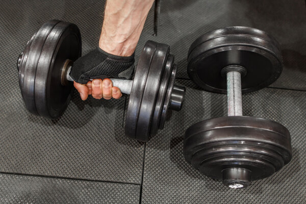 Two dumbbells on gym floor, one held by mans hand