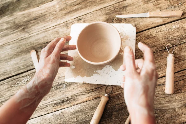 Tangan di atas mangkuk tanah liat di atas meja kayu, artisan pov — Stok Foto