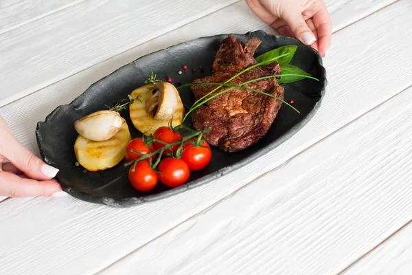 Las manos ponen la plancha con el bistec a la mesa, copyspace — Foto de Stock