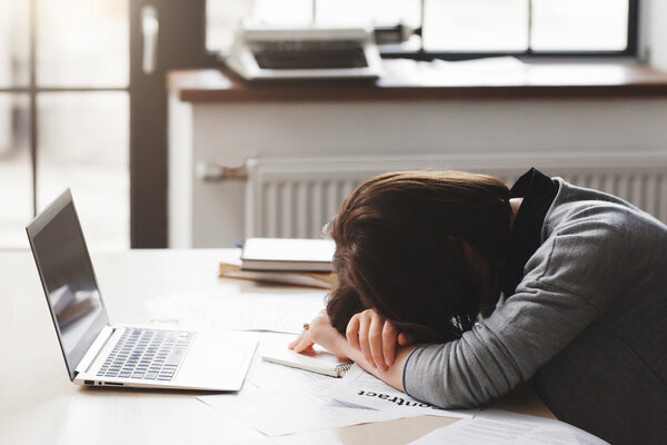 Молодая уставшая женщина спит за рабочим столом
