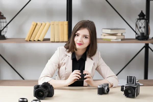 Smiling woman sitting at table with cameras — Stock Photo, Image