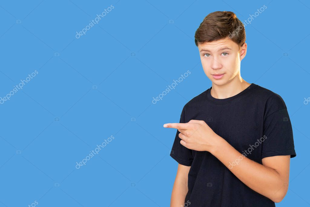 Special offer. Advertising background. Solution idea. Portrait of confident teen boy in black t-shirt presenting invisible product information pointing finger at copy space isolated on blue.