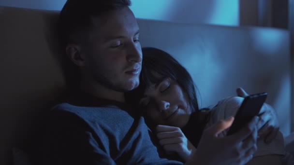 Kuscheliges Pärchen nächtigt mit Handy im Bett — Stockvideo