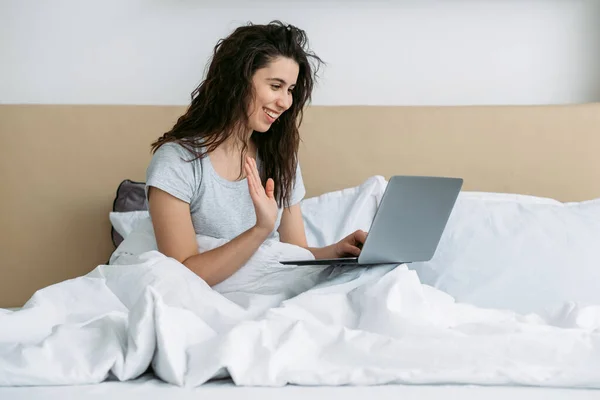 Ochtend video oproep gelukkig vrouw groeten laptop bed — Stockfoto