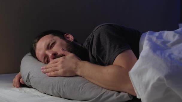 Спокойной ночи, уставший мужчина засыпает в уютной постели — стоковое видео