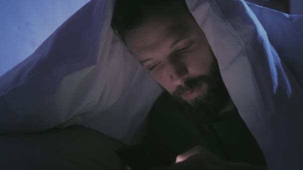 Nacht online amüsierte Mann mit Telefon unter Decke — Stockvideo